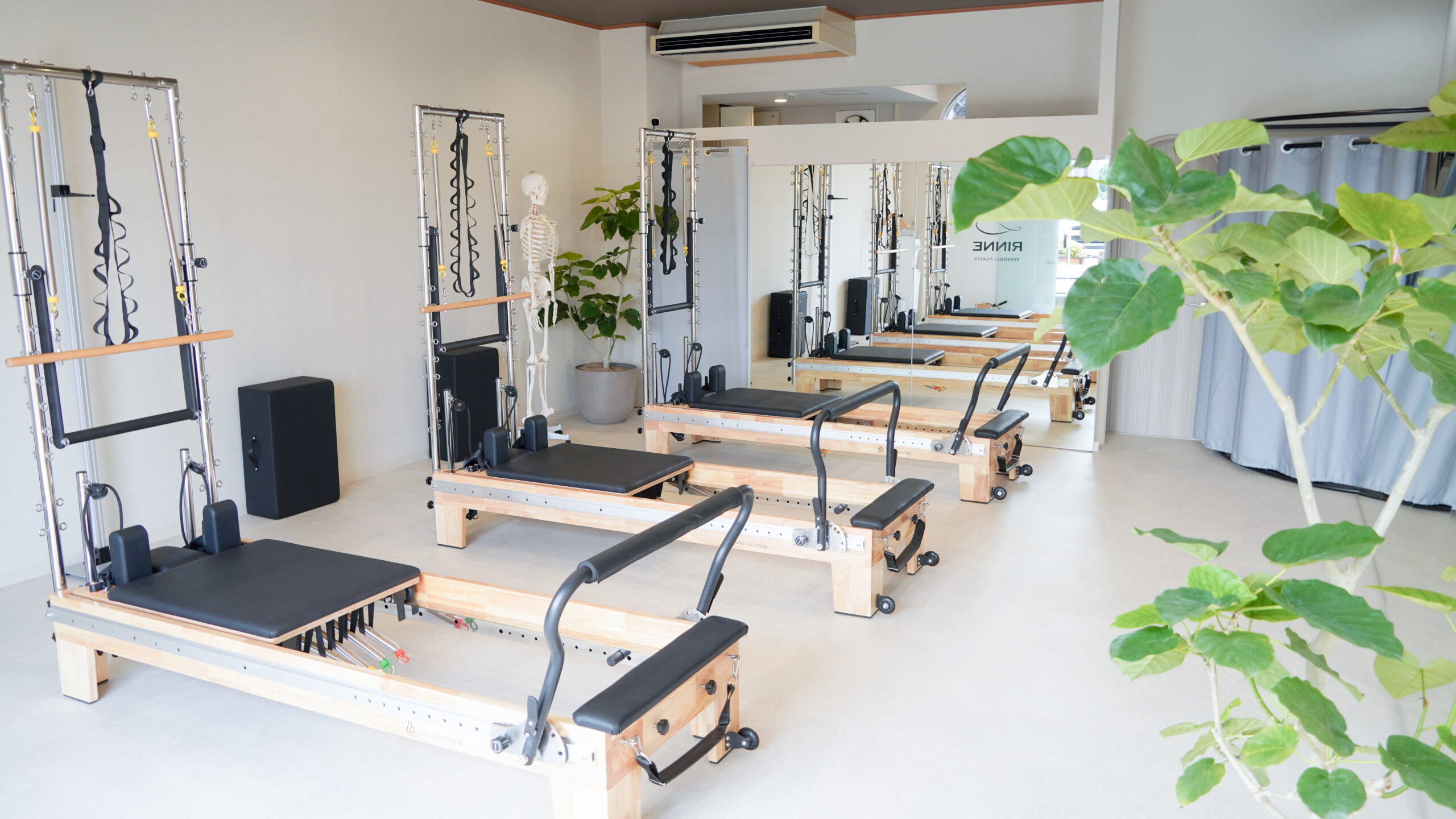 ピラティスマシンと大きな鏡、観葉植物のある明るい店舗空間
